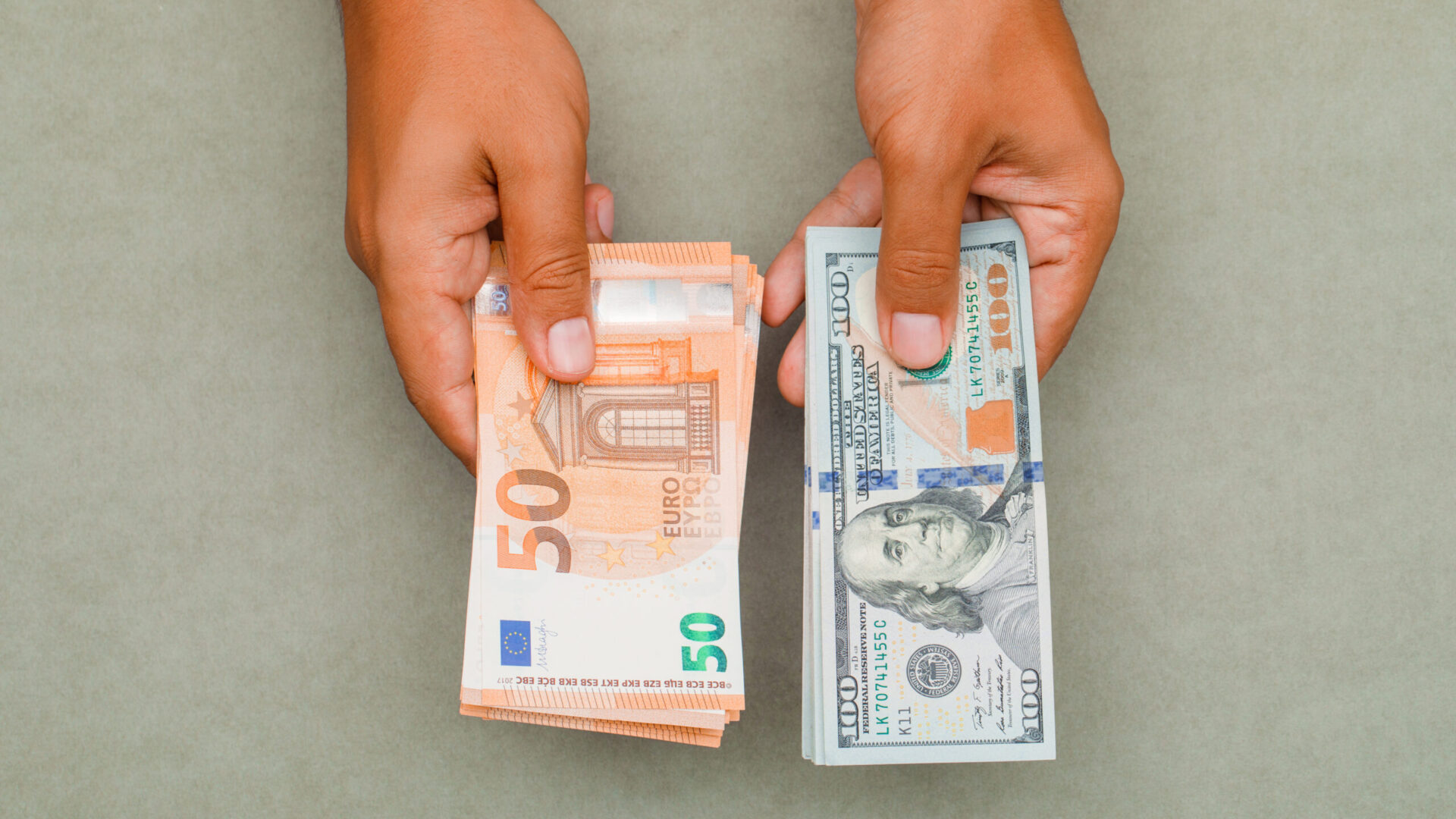 Financial concept on greenish grey background flat lay. hands holding dollars and euros.